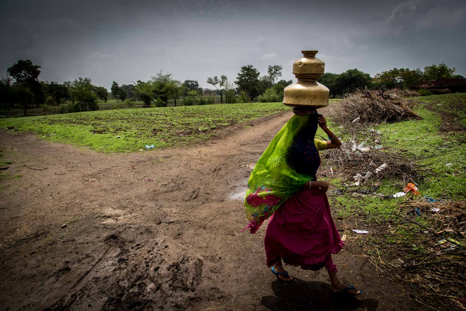 A person carrying a container on their head across a field.