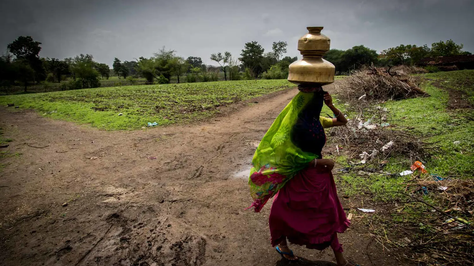 A person carrying a container on their head across a field.