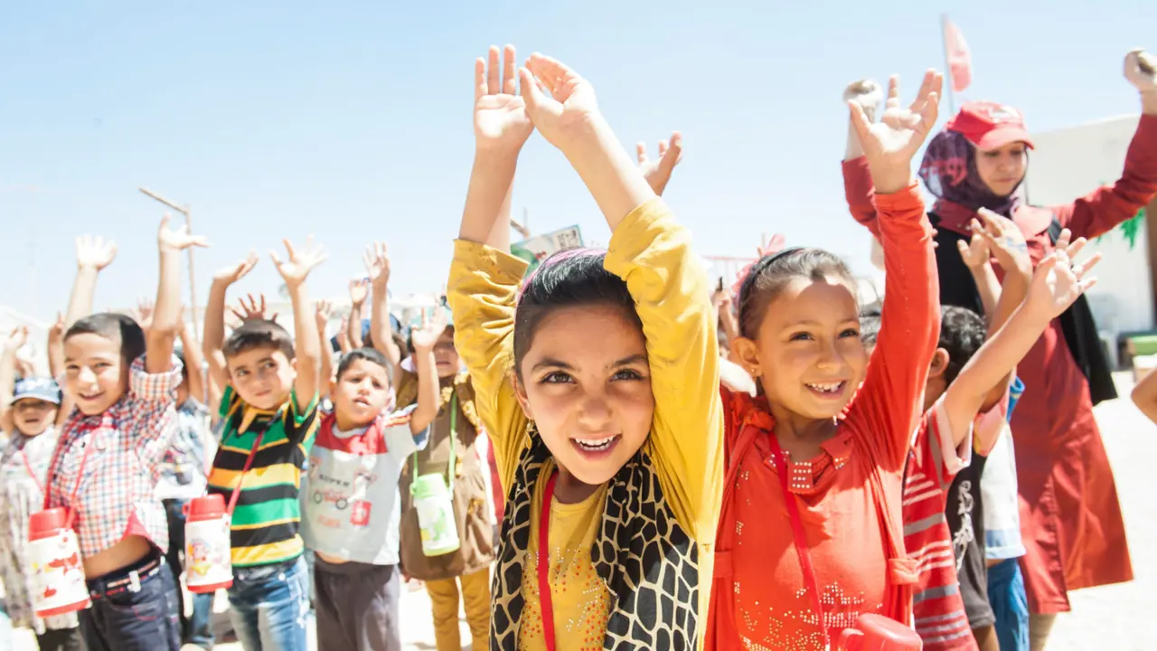 A group of children smiling and holding their hands high in the air