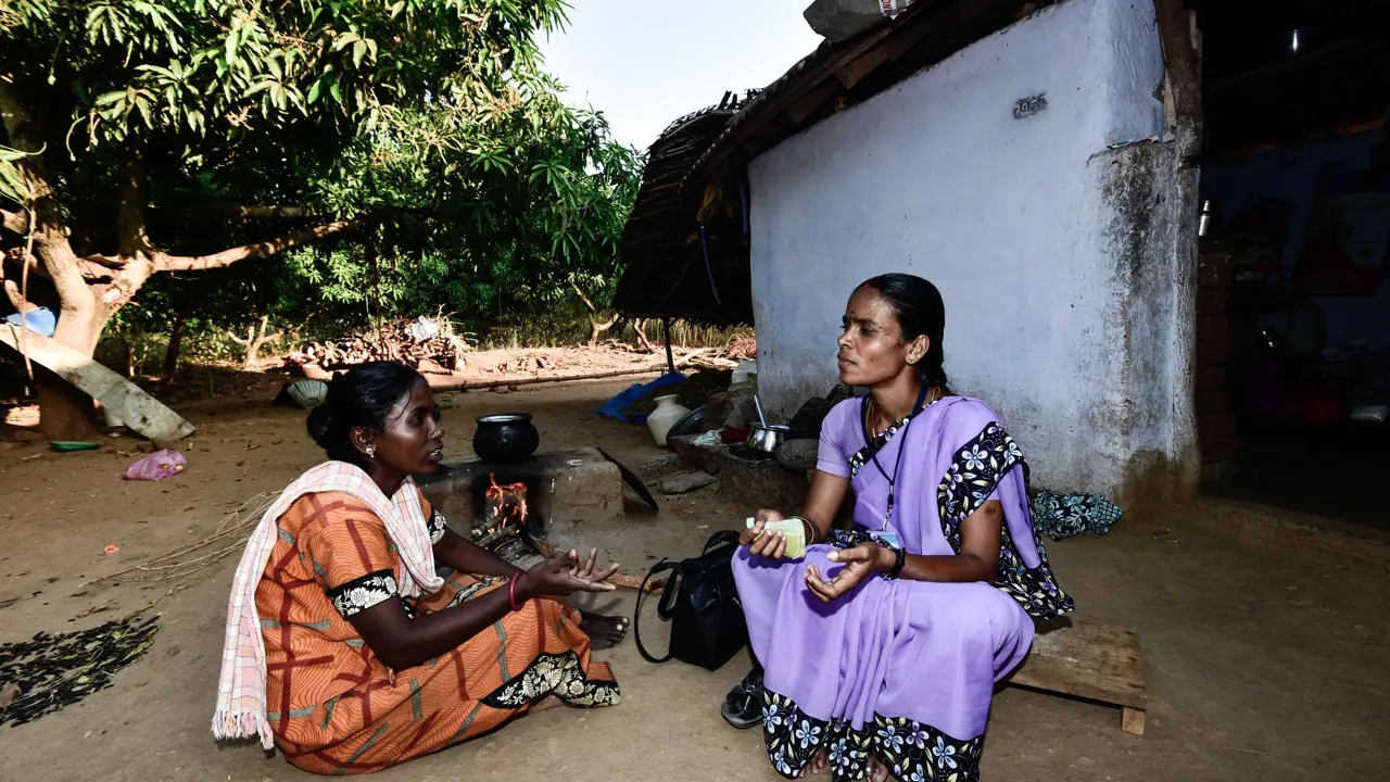 Two women sitting on the ground next to a pot on the fire talking