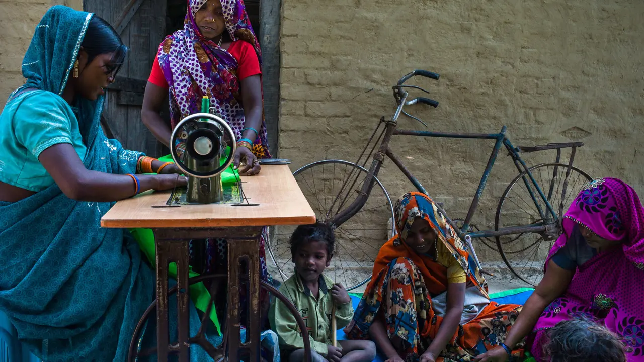 Women working on a sewing machine surrounded by children