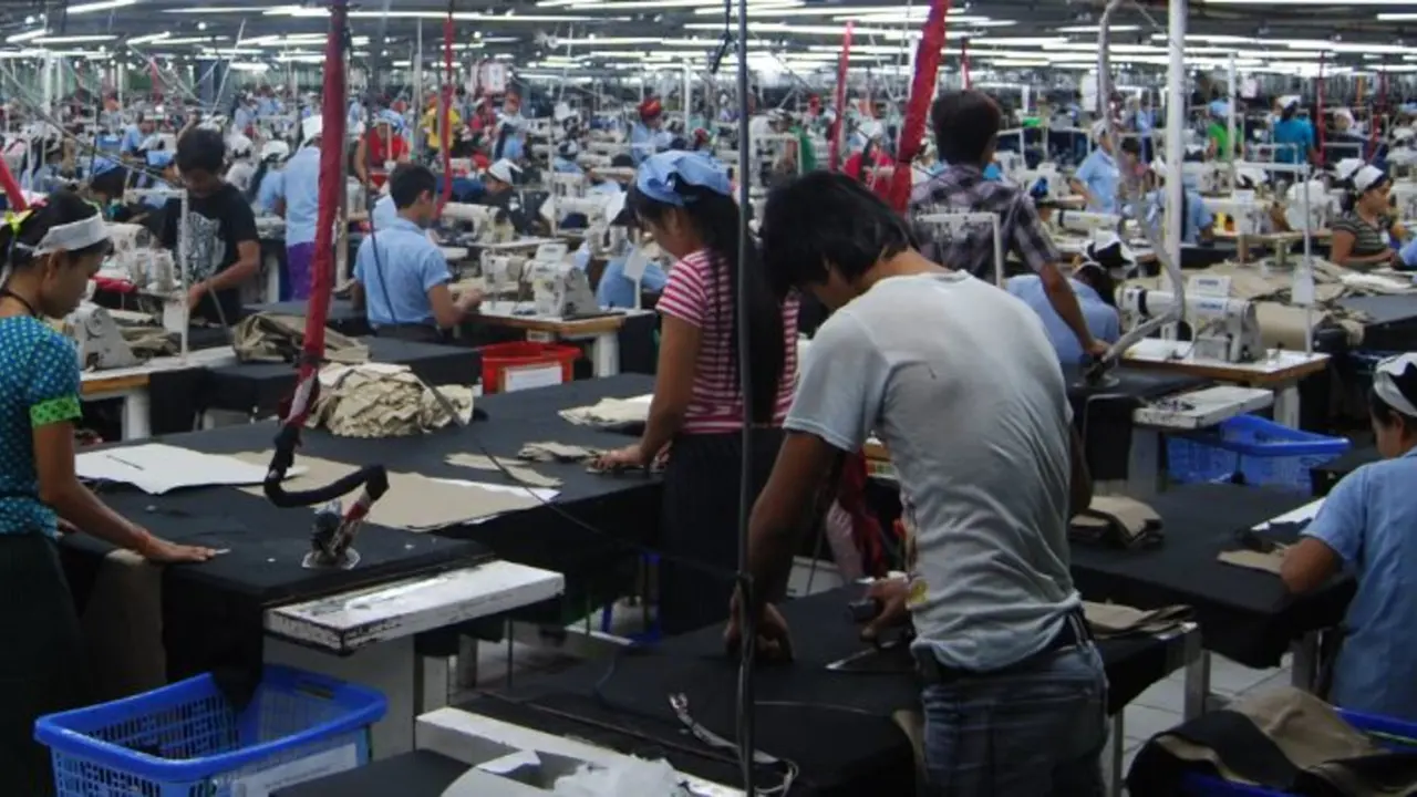 A crowded factory with many workers at workstations with sewing machines