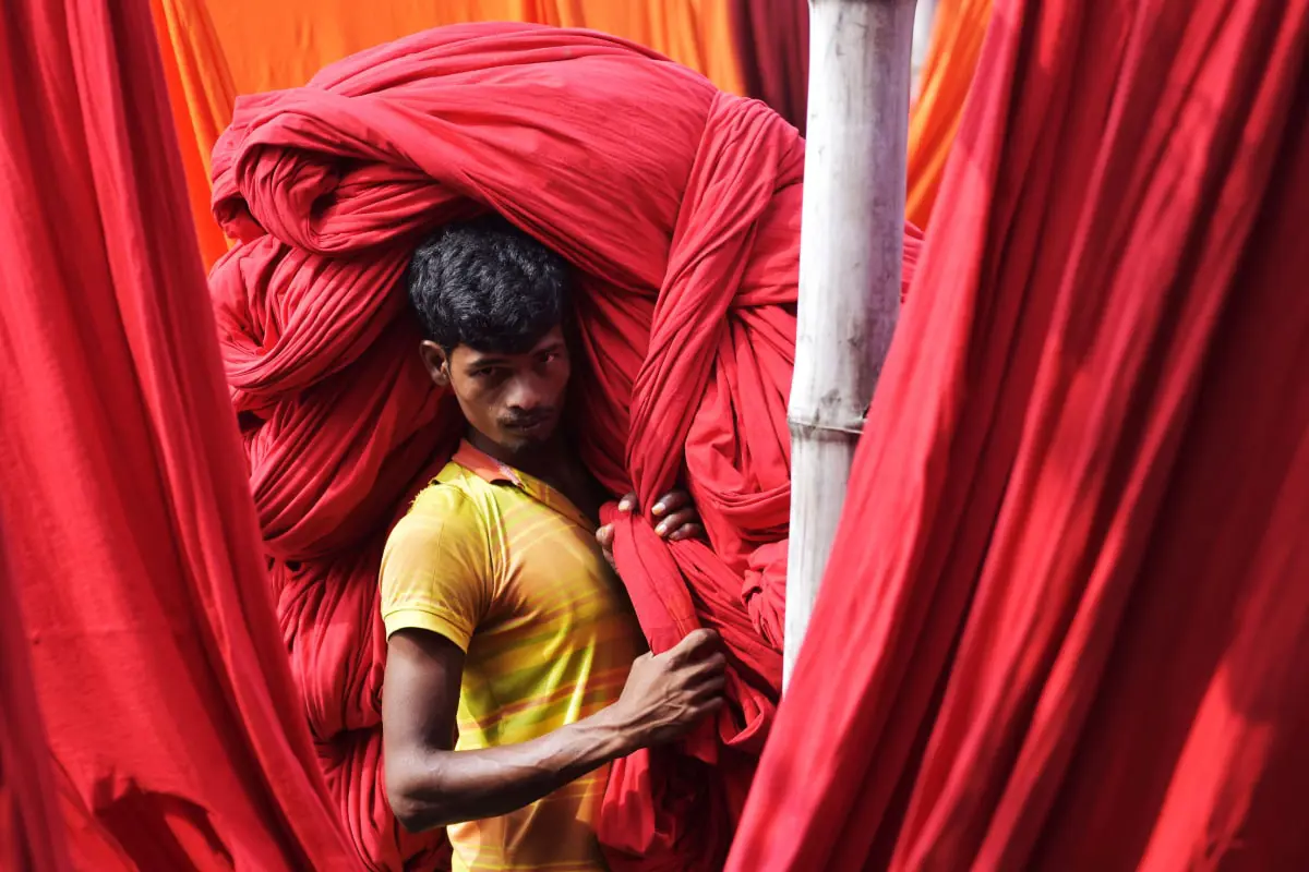 A man carrying a large pile of red coloured fabric