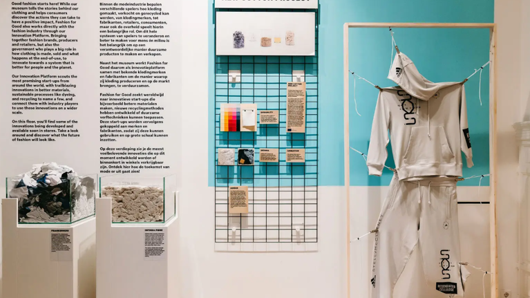 An informative display of items laid out in an exhibition style, including two glass containers of raw fabric materials, a tracksuit, and a colour chart