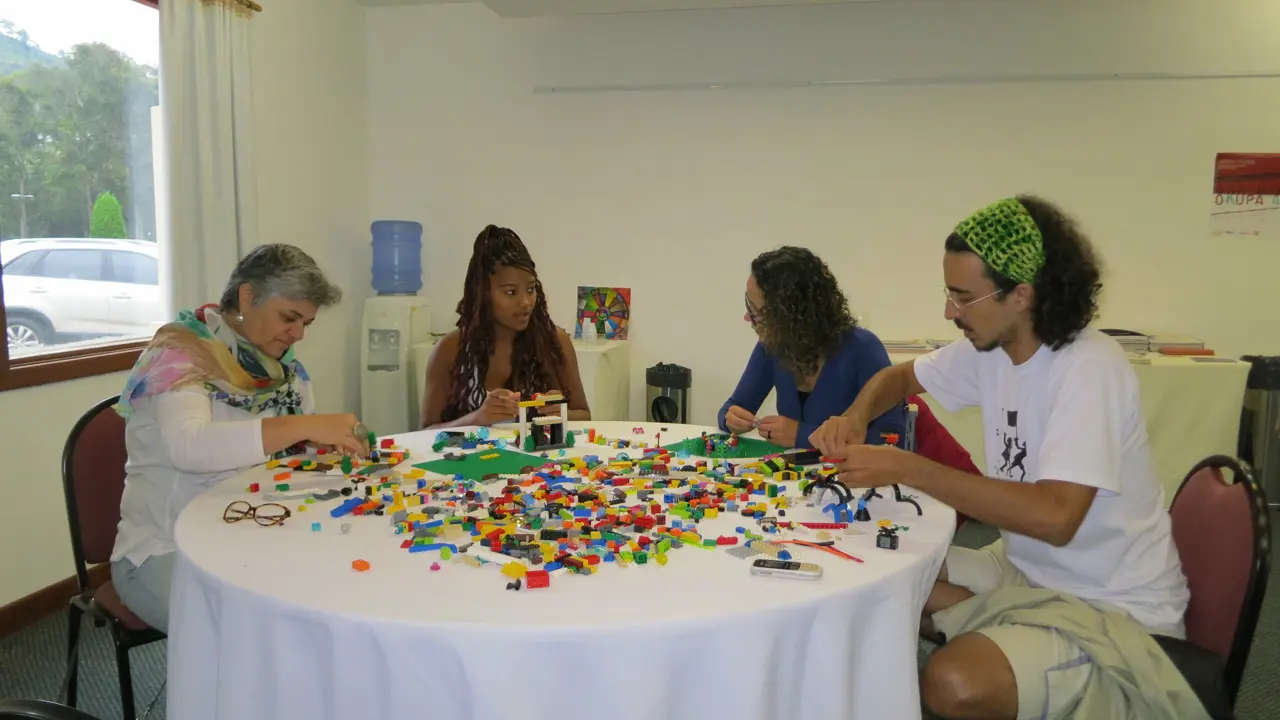 A group of people sitting around a table which is covered in toy building bricks, they are making models