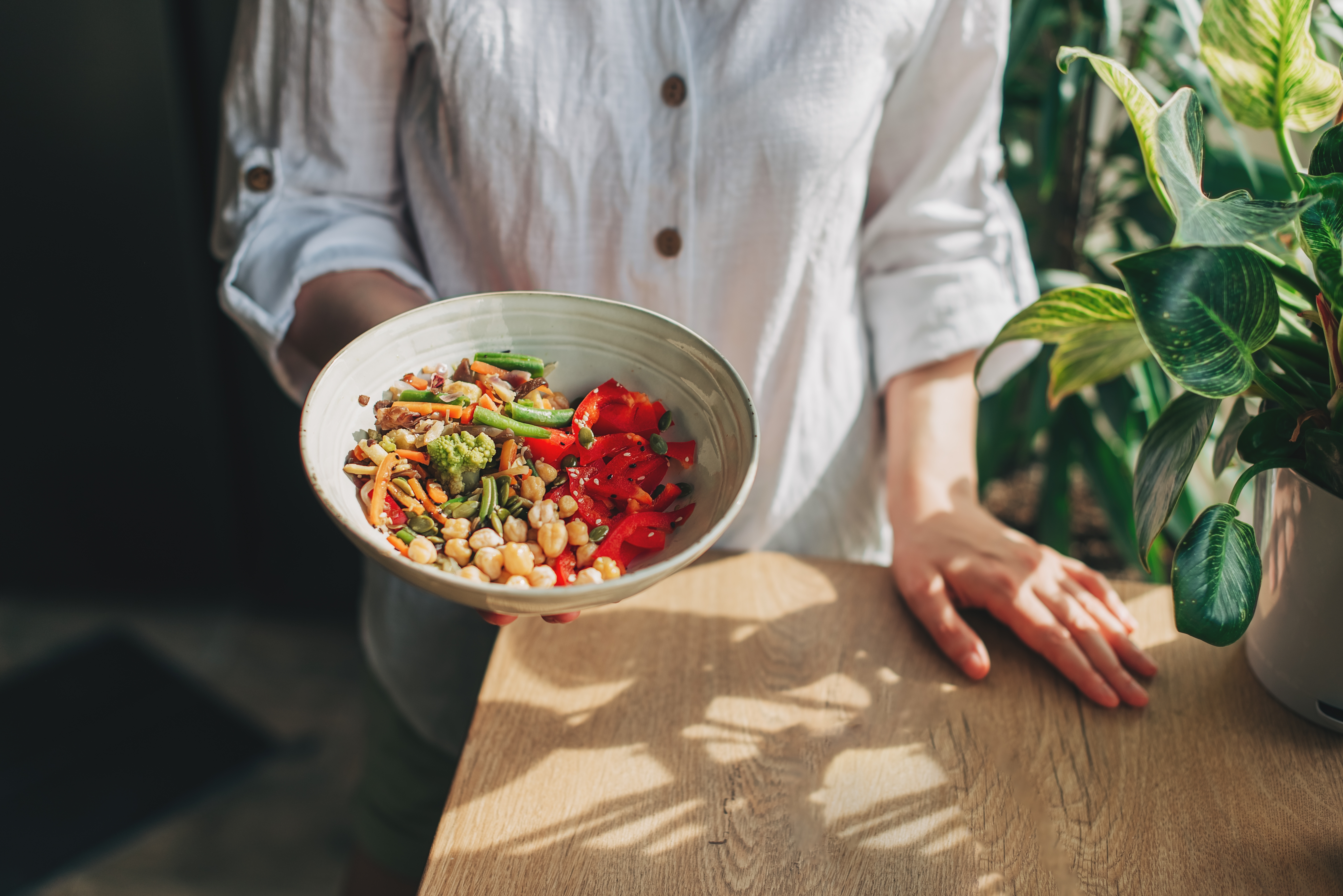 A close up of a person holding out a bowl of food consisting of nuts and brightly coloured vegetables - green beans, red peppers and carrots.