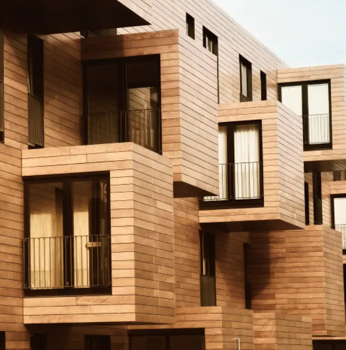 The side of a building with a modular look, clad in wood with many small balconies and glass double doors