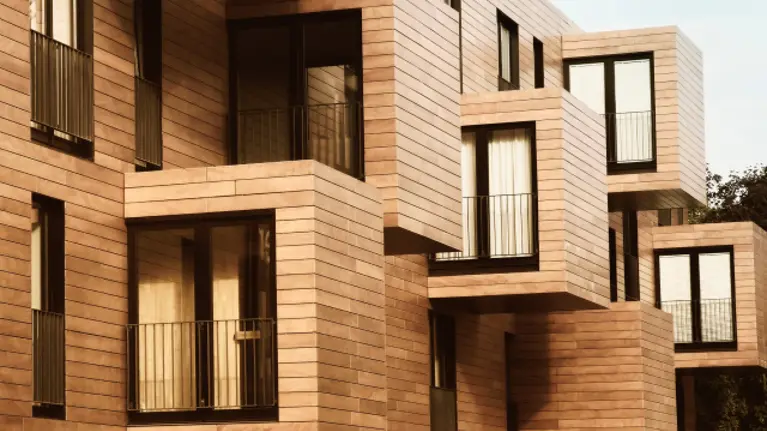 The side of a building with a modular look, clad in wood with many small balconies and glass double doors