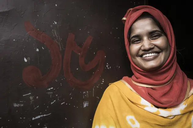 A woman smiling at the camera in bright clothing against a dark wall