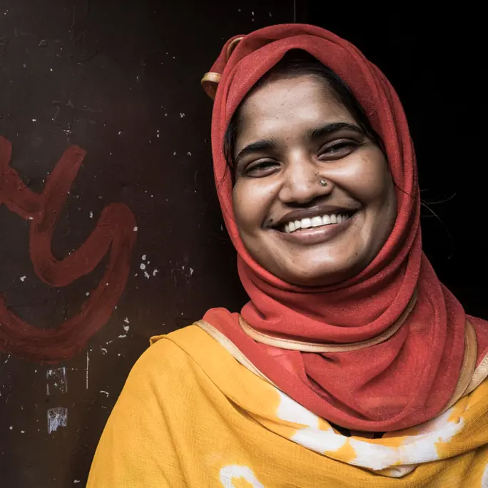A woman smiling at the camera in bright clothing against a dark wall close up