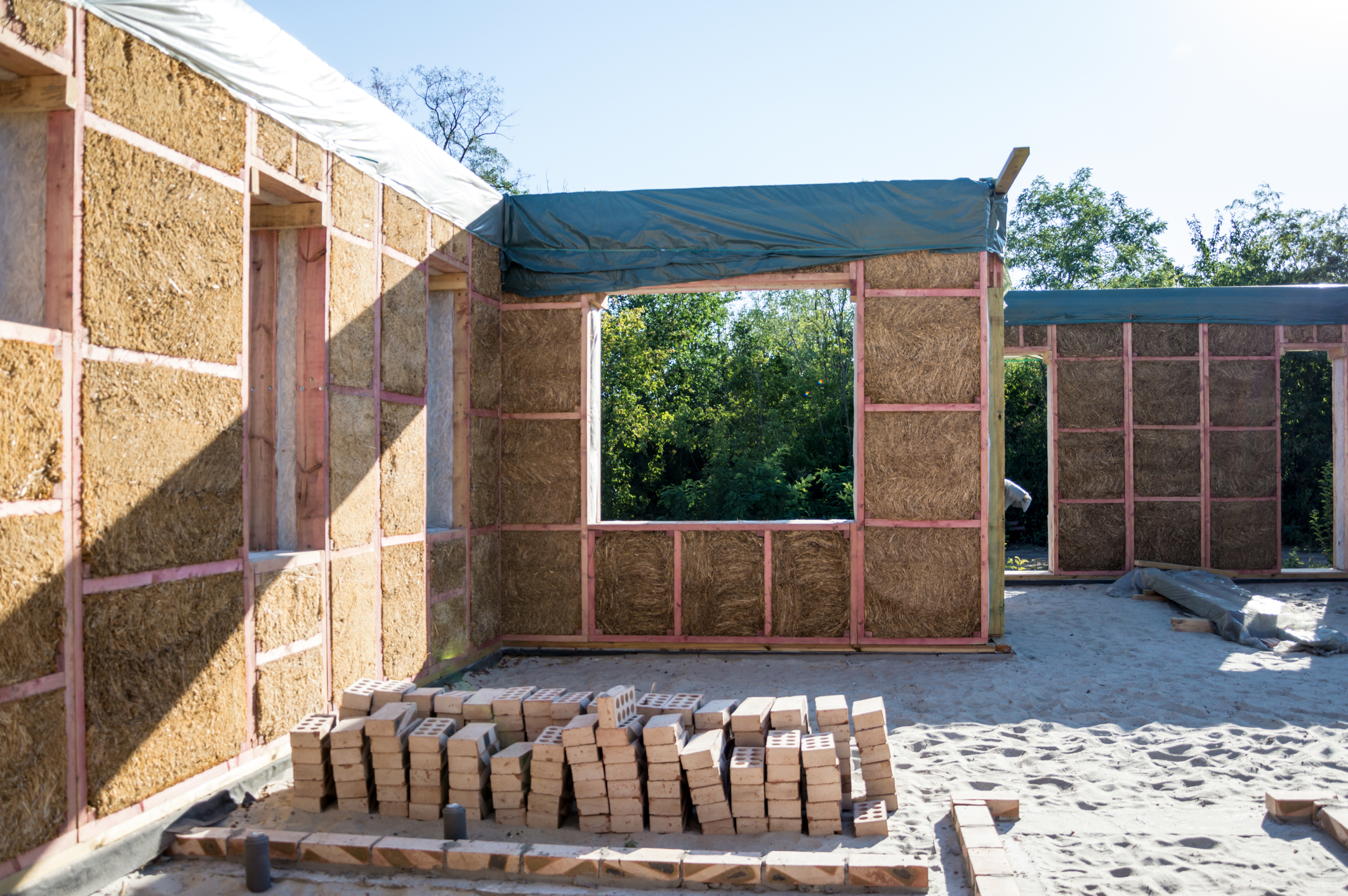 Walls in the process of being built, the wooden frame and internal insulation is visible and there are loose bricks stacked up in the foreground.