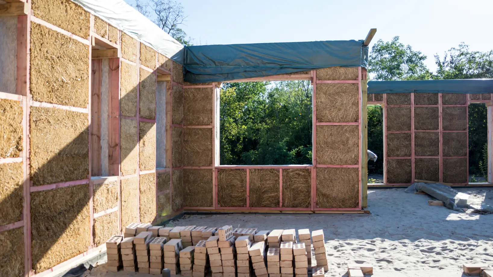 Walls in the process of being built, the wooden frame and internal insulation is visible and there are loose bricks stacked up in the foreground.
