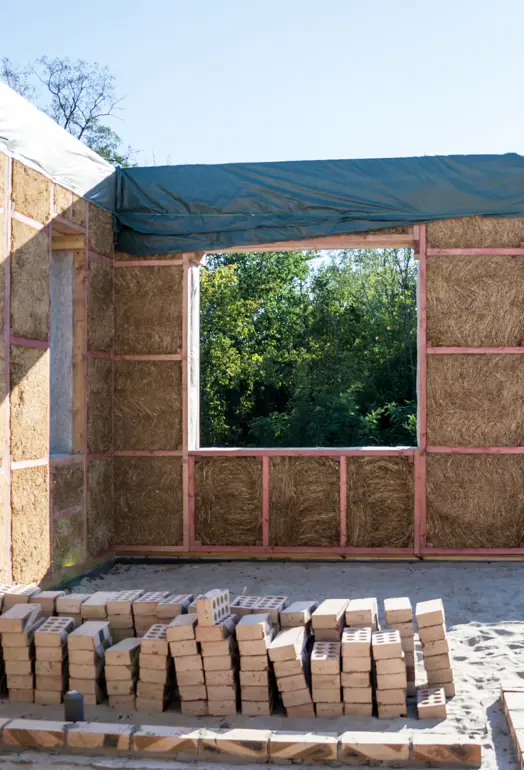 Walls in the process of being built, the wooden frame and internal insulation is visible and there are loose bricks stacked up in the foreground.