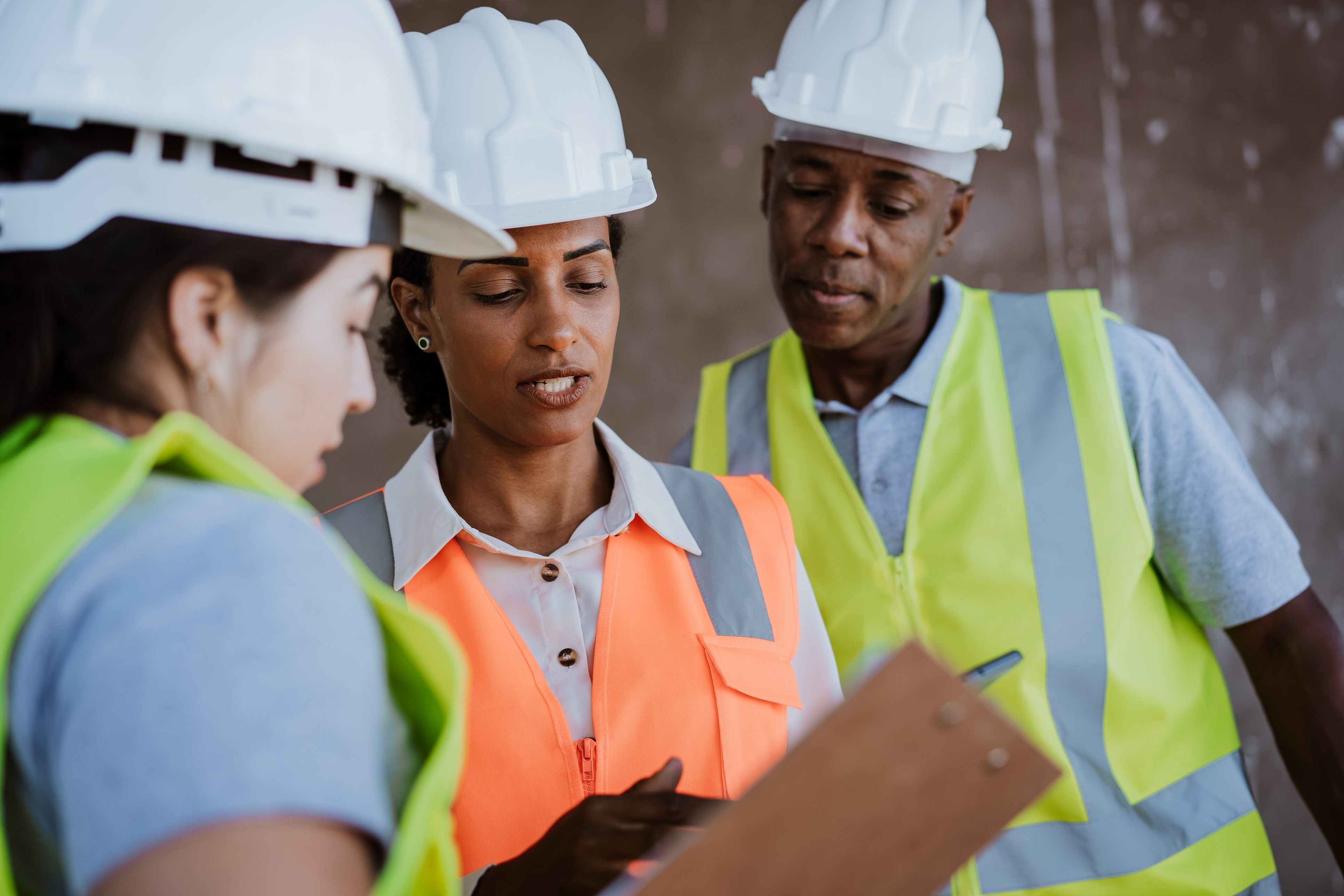 Three people wearing hard hats and high visibility vests reading from a clipboard