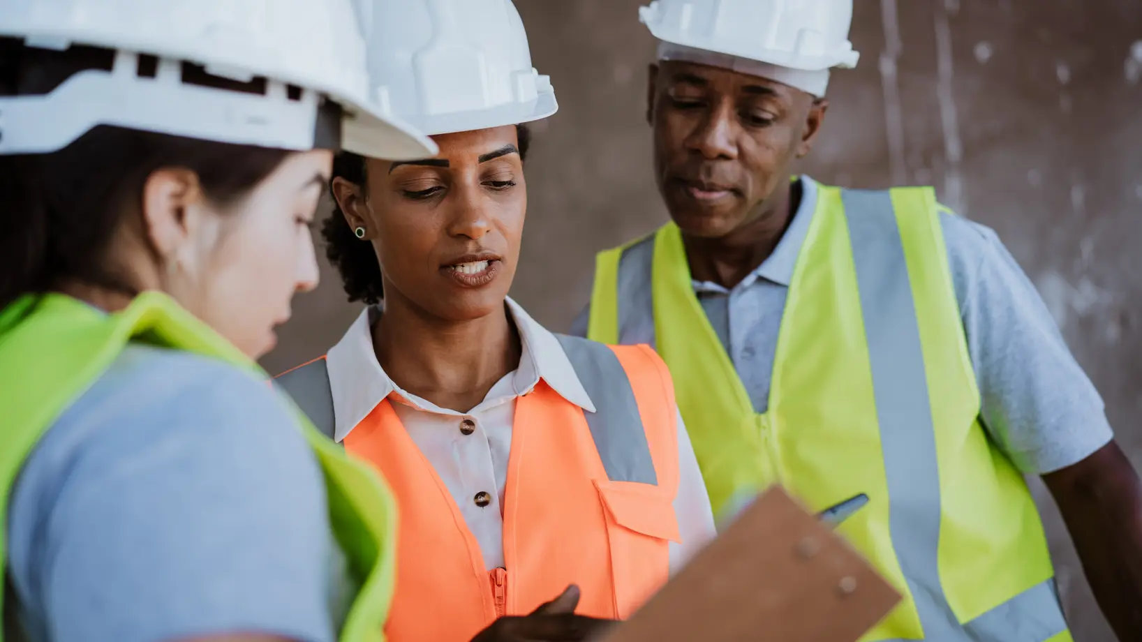Three people wearing hard hats and high visibility vests reading from a clipboard