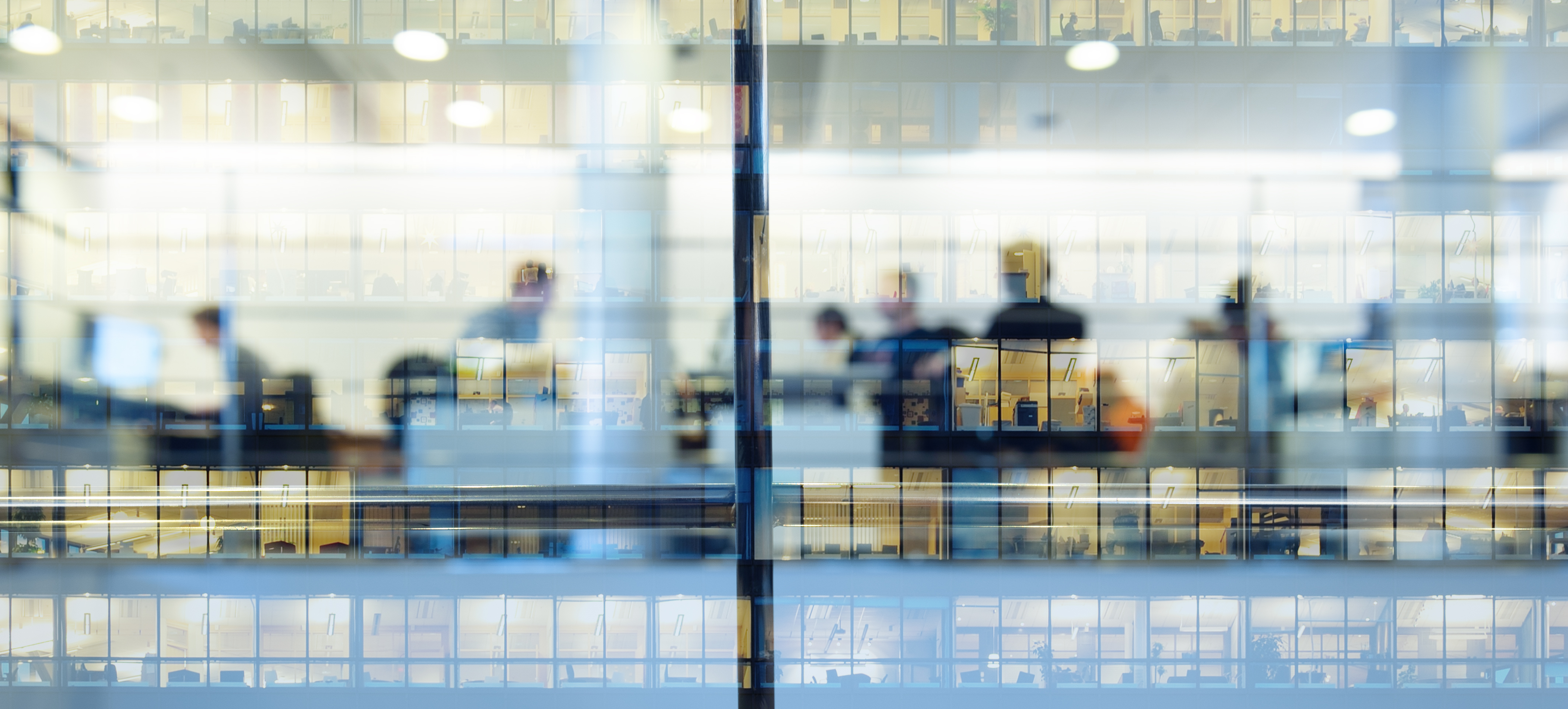 A view of blurred figures in an office block distorted by the reflections on the window